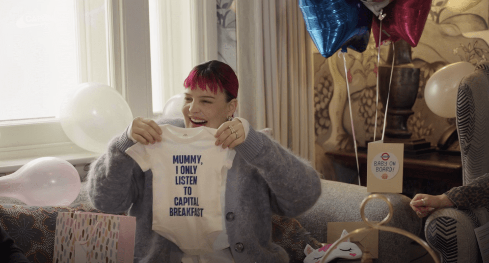 Anne-Marie holding a baby onesie that says "Mummy, I only listen to Capital Breakfast."