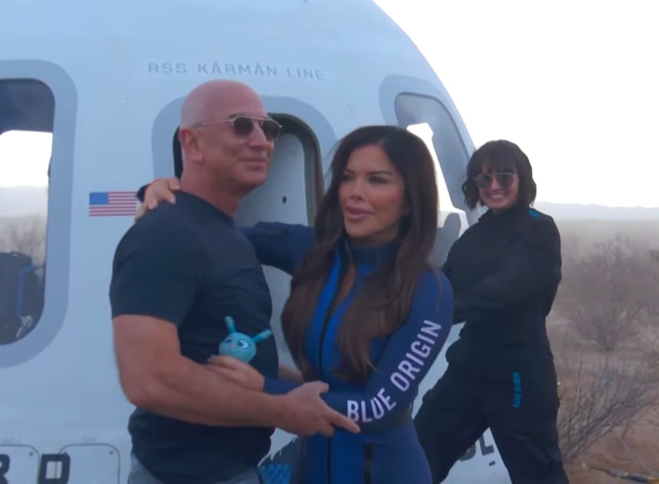 Jeff Bezos, Lauren Sanchez, and another woman in Blue Origin flight suits stand in front of a spacecraft.