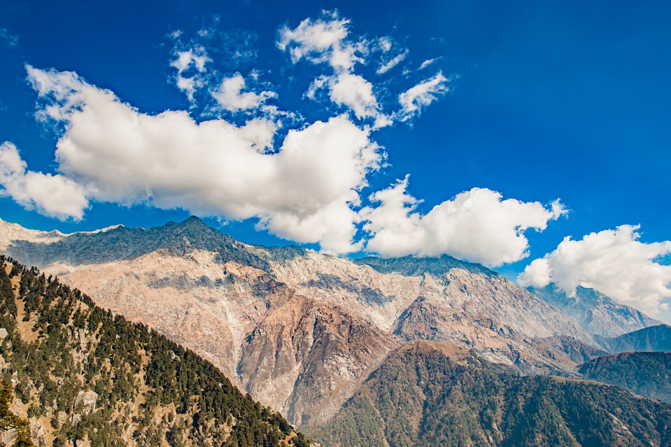 Dhauladhar mountain range under a partly cloudy blue sky.