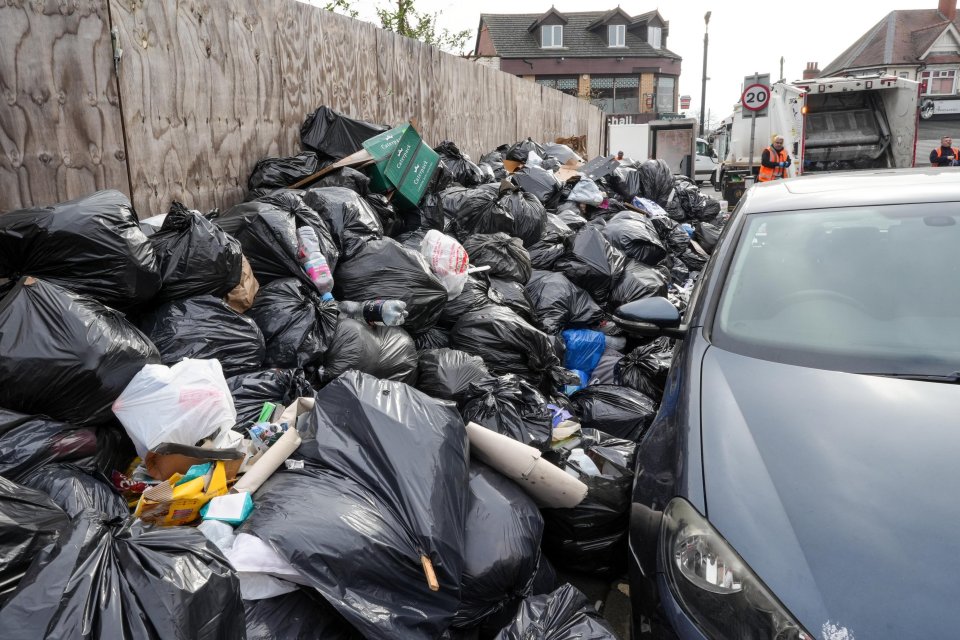 A large pile of black garbage bags overflowing with refuse next to a car.