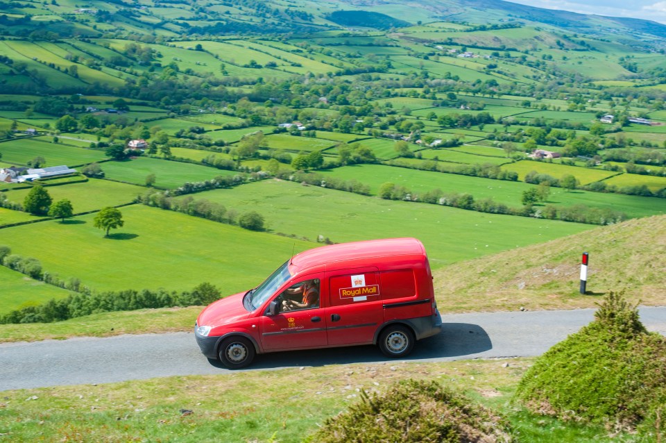 Red Royal Mail van driving on a country road.