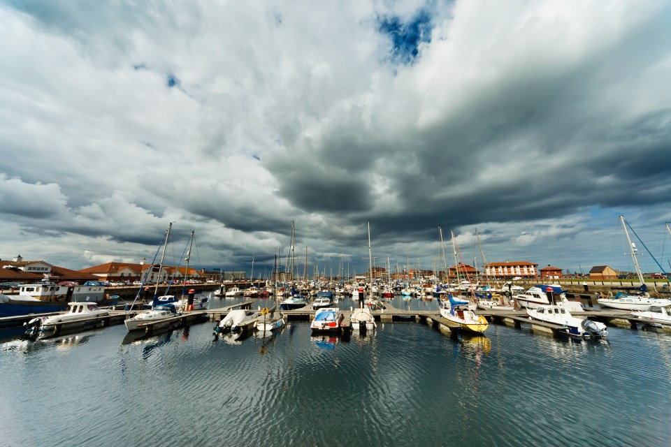 Boats moored in a harbor under a cloudy sky.