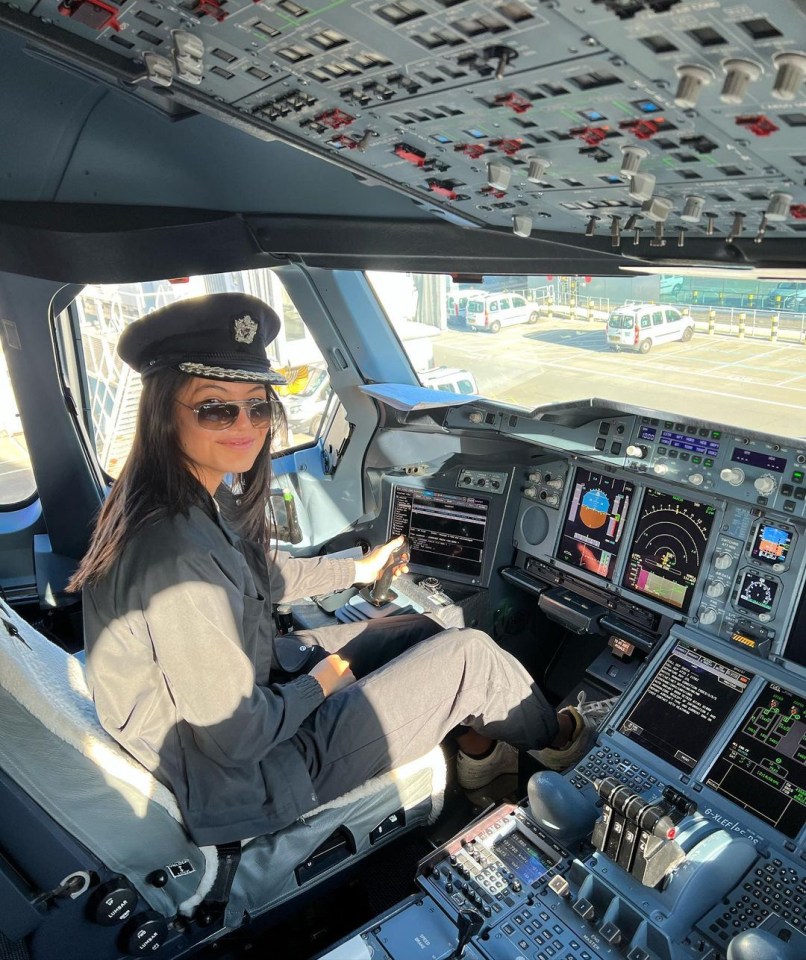 Woman in pilot uniform seated in airplane cockpit.