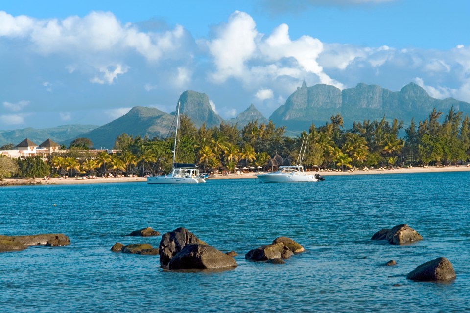 Beachfront hotel with boats and mountains in the background.