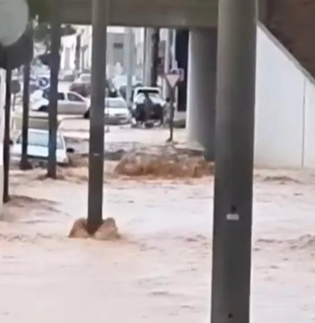 Floodwaters inundate a street, partially submerging cars.