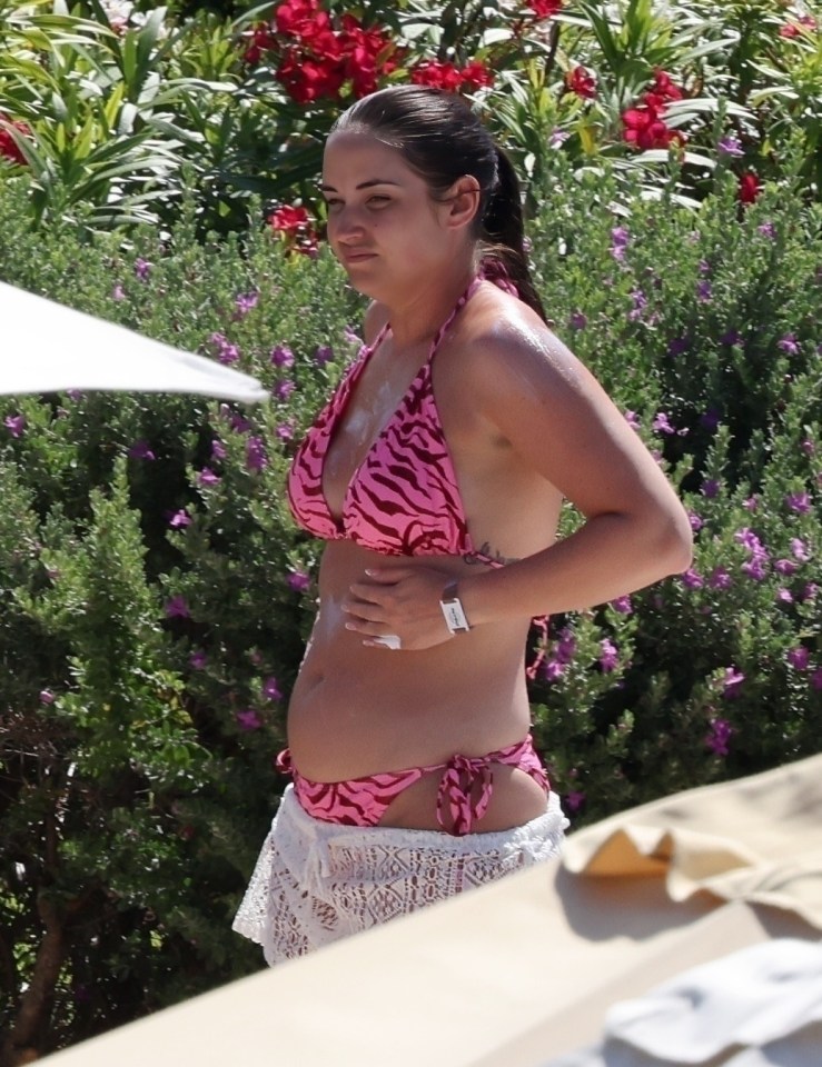 Jacqueline Jossa applying sunscreen while wearing a pink bikini and white cover-up.