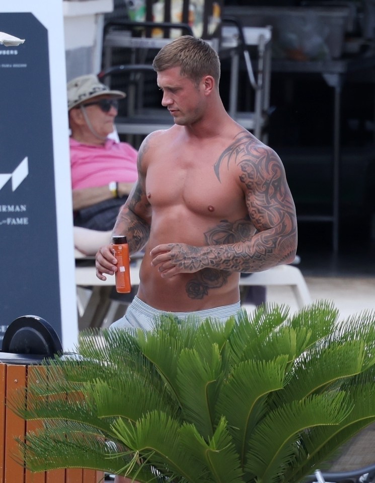 Dan Osborne, shirtless and holding sunscreen, at a resort.