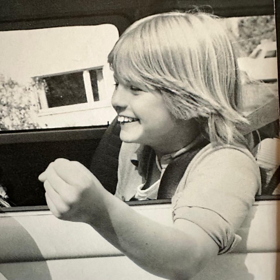 Black and white photo of a young girl smiling in a car.