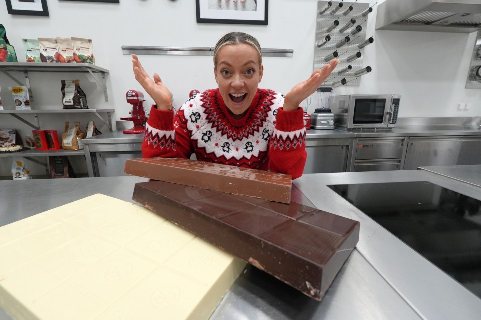 Woman in a Christmas sweater showing off large chocolate bars.