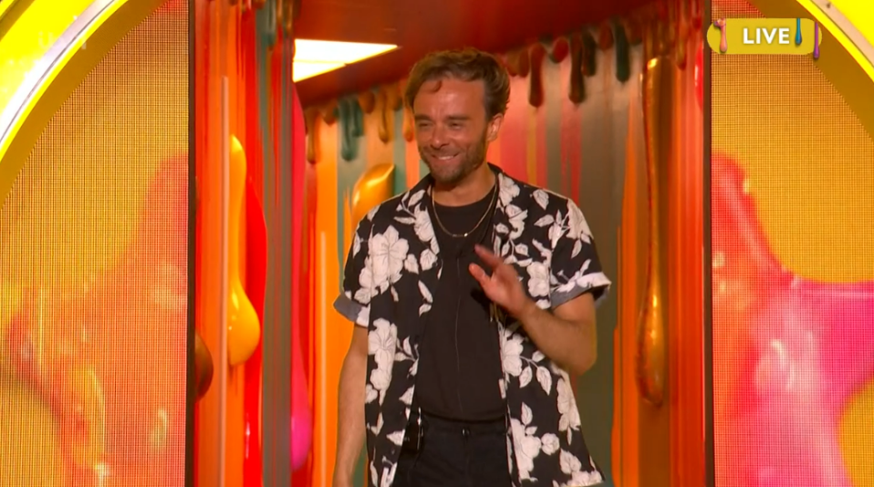 Man in floral shirt waving in colorful hallway.