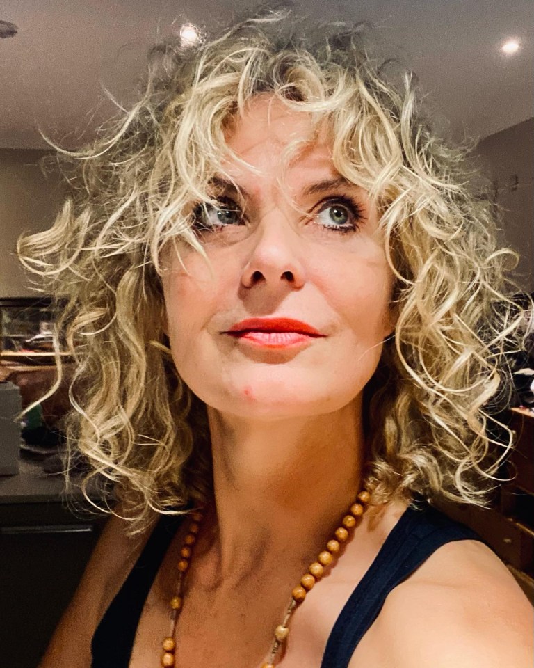 Close-up portrait of a woman with blonde, curly hair and a beaded necklace.