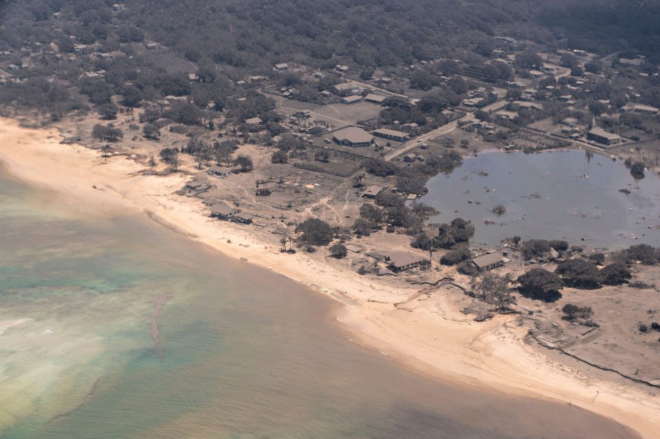 Aerial view of ash-covered coastal village in Tonga after volcanic eruption.