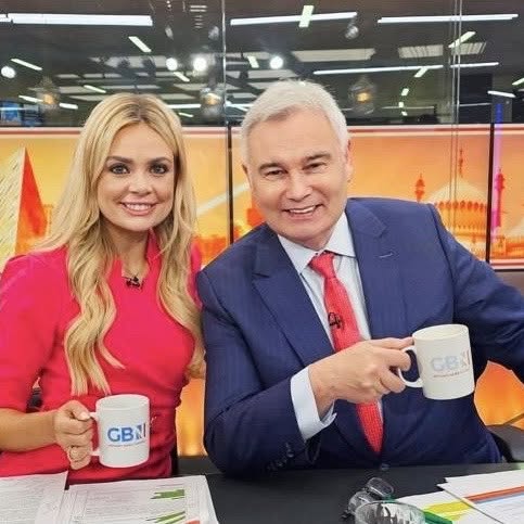 Eamonn Holmes and a female co-host holding GB News mugs on set.