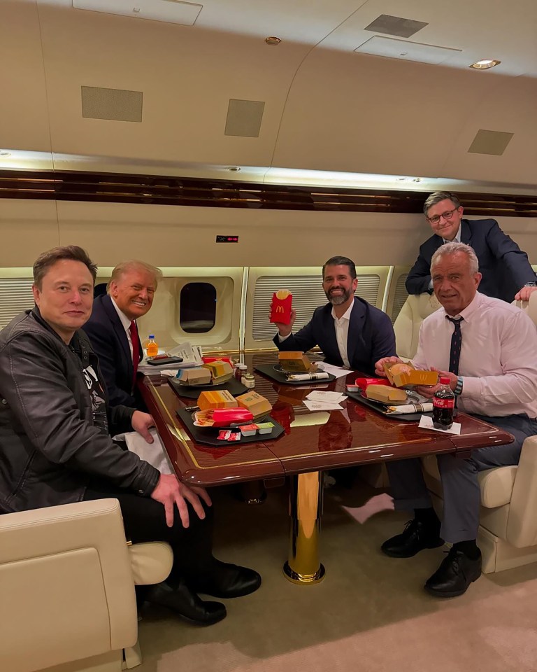 Elon Musk, Donald Trump, Donald Trump Jr., Mike Johnson, and Robert F. Kennedy Jr. seated at a table on a private jet, eating McDonald's.