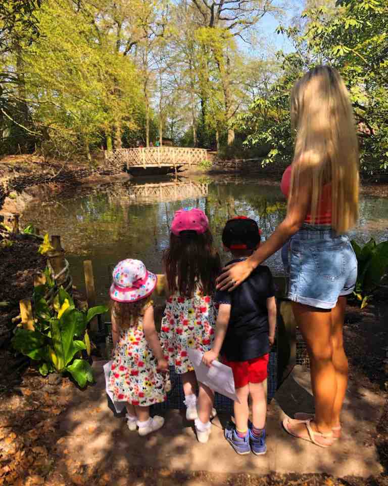 A mother and her three children stand by a pond in a wooded area.