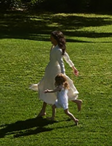 Meghan Markle and a young child running on a grassy lawn.