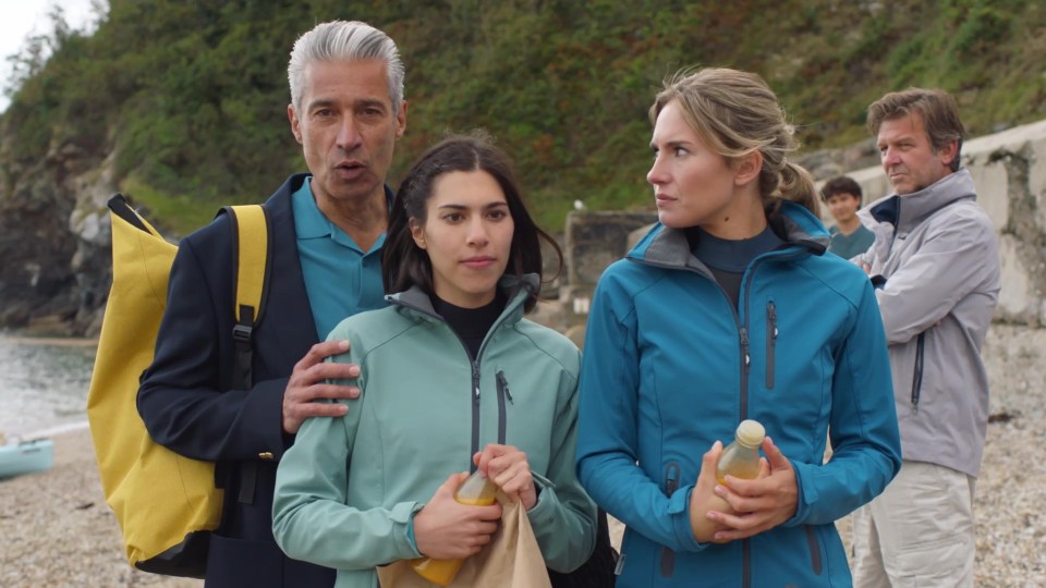 A group of people standing on a beach, looking concerned.