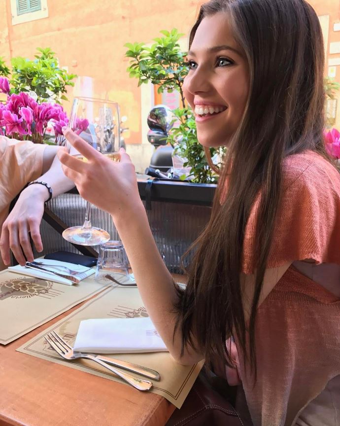 Woman sitting at an outdoor cafe table, holding a glass of wine.