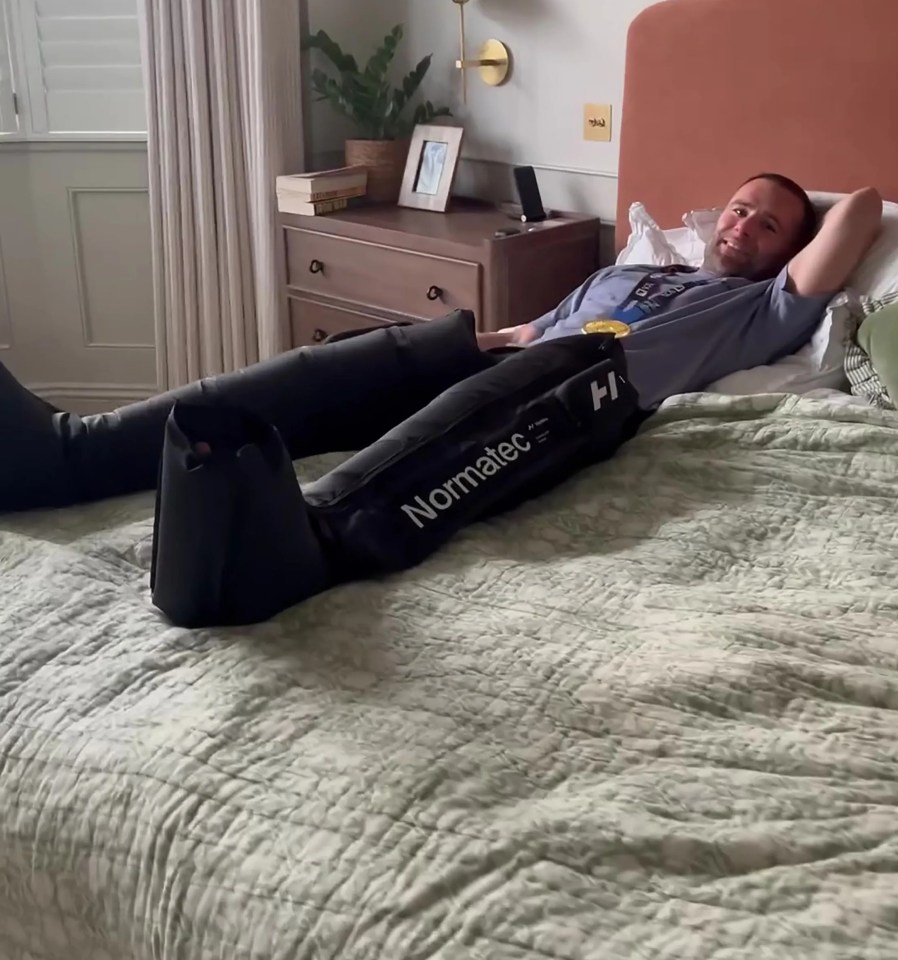 Man wearing a marathon medal and recovery boots in bed.