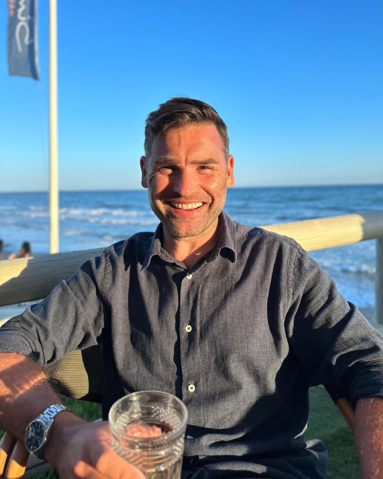 Man smiling at the beach holding a glass.