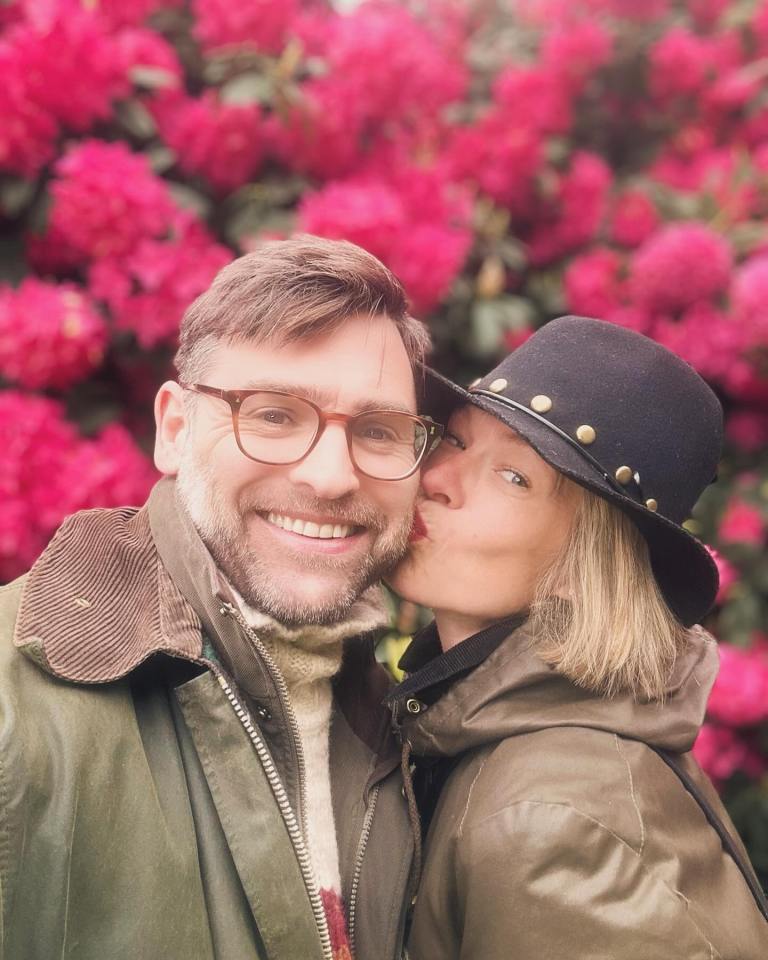 A woman kissing a man on the cheek in front of pink flowers.