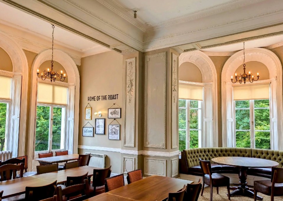 Interior of a restaurant with large windows, wooden tables, and chandeliers.