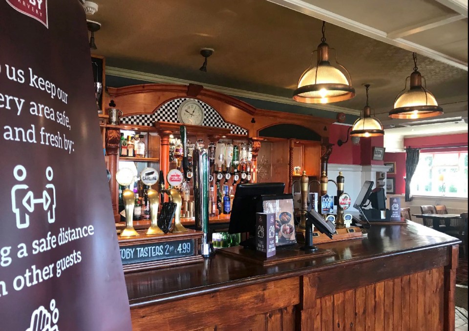 Pub bar with beer taps and social distancing sign.