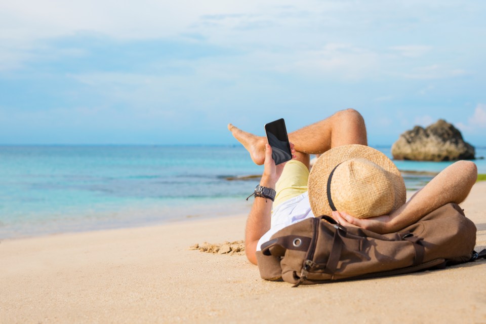 Man relaxing on a beach, using his smartphone.