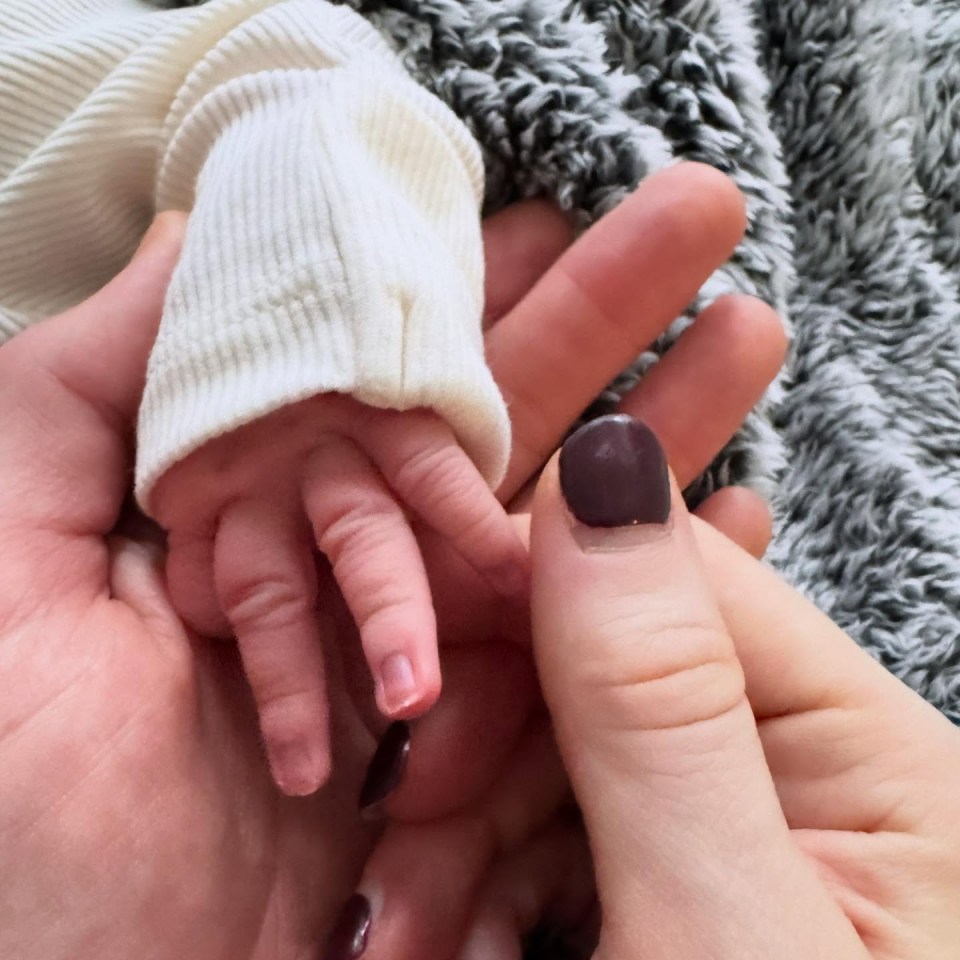 A newborn's hand held by an adult's hand.