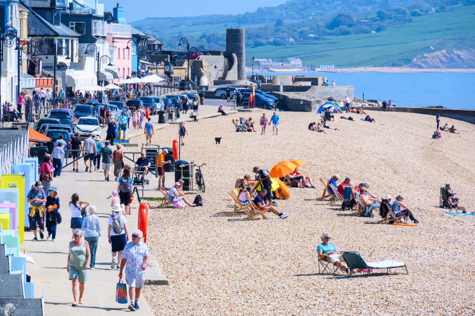 Sunny beach scene in Lyme Regis, Dorset, UK, with people enjoying the weather.