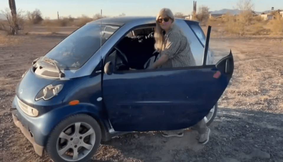 Woman exiting a small blue car in a desert landscape.