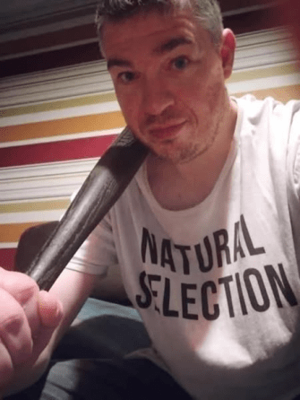 Man holding a bat, wearing a "Natural Selection" shirt.