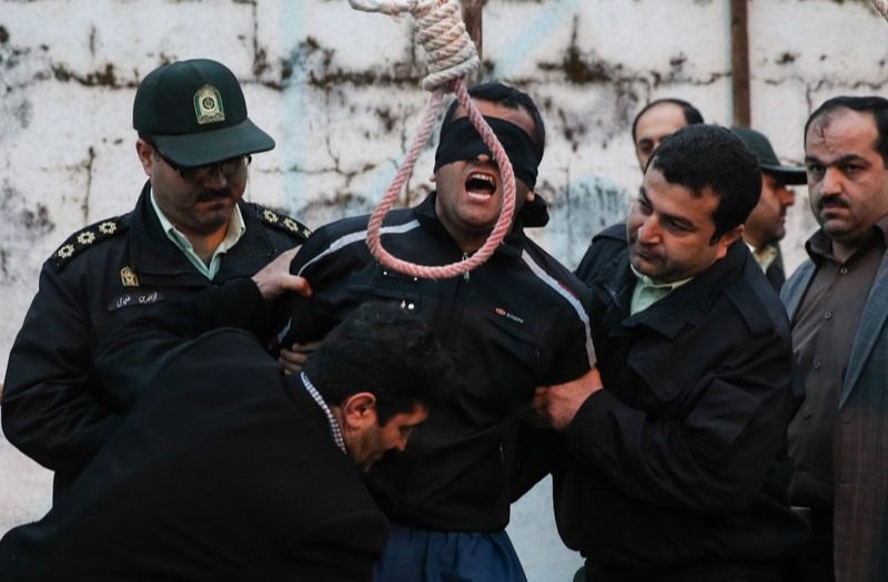A blindfolded man about to be hanged by police officers.