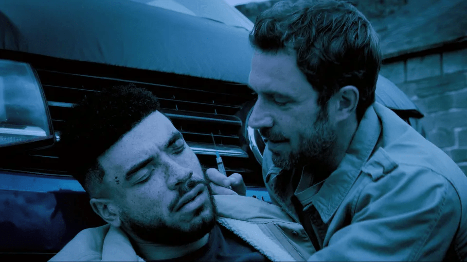 Man injecting another man near a car.