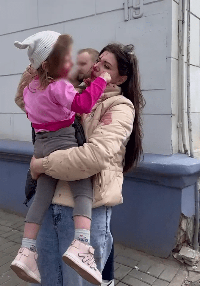 Woman holding a child, both with blood on their clothes.