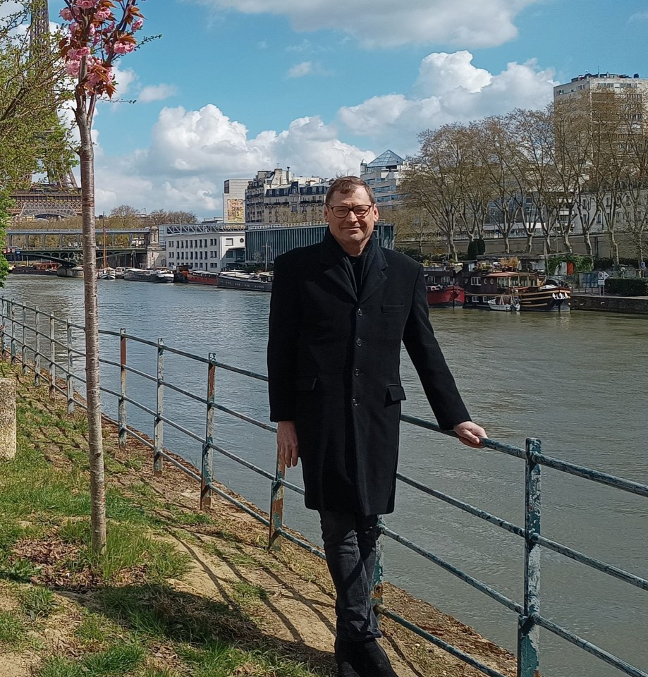 Man in black coat standing by a river in Paris.