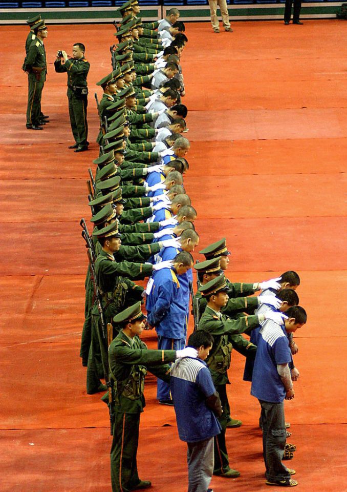 Soldiers escorting a line of prisoners bowing their heads.
