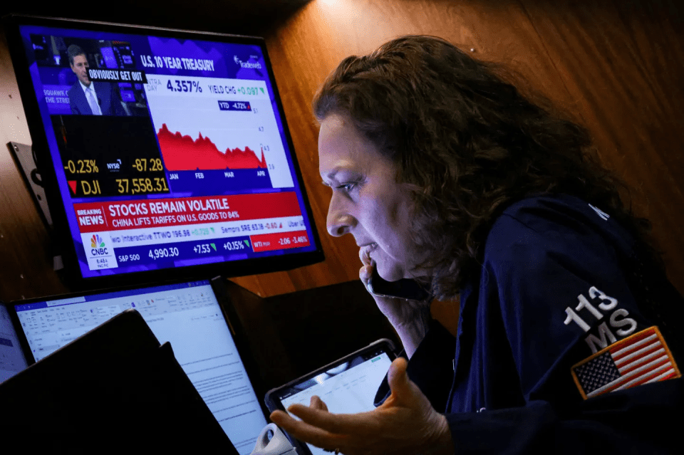 A woman on the phone looks at stock market data on multiple screens.
