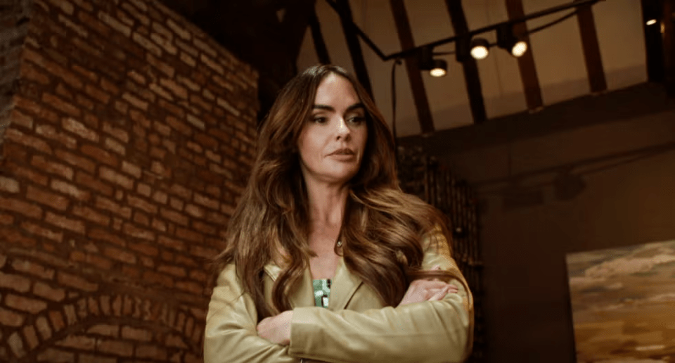Woman with long brown hair standing with her arms crossed in a room with a brick wall.