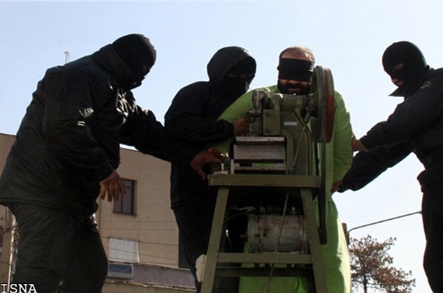 A blindfolded man being held by three masked individuals near a machine.