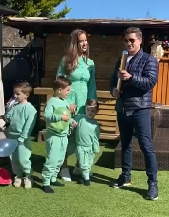 Family with three young children in matching mint green outfits in their backyard.