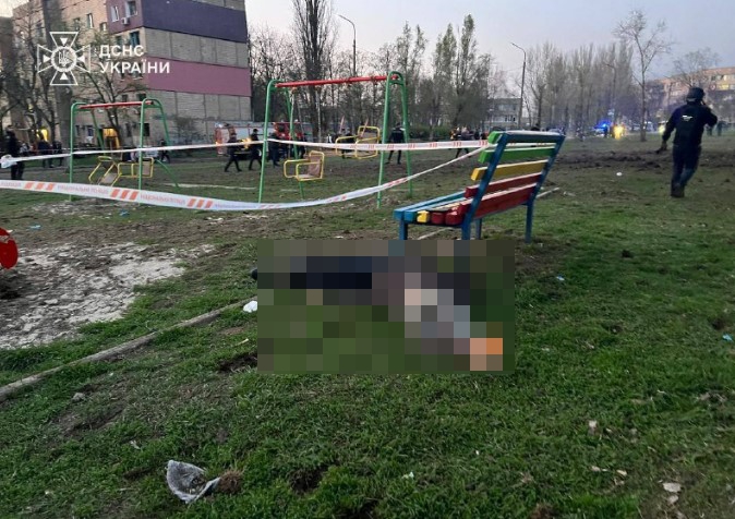Playground with police tape and a blurred figure on the ground.