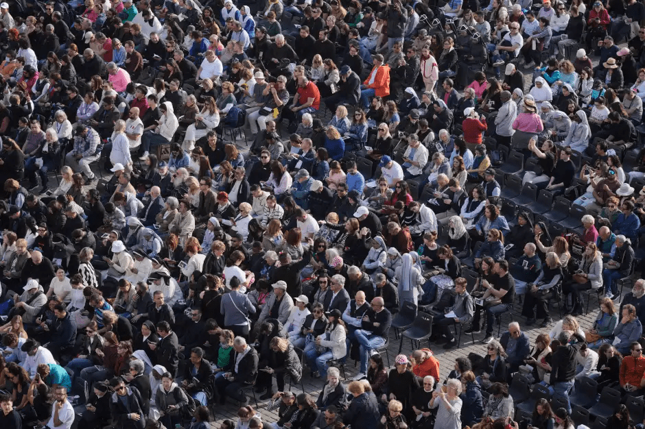 Large crowd of people sitting outdoors.