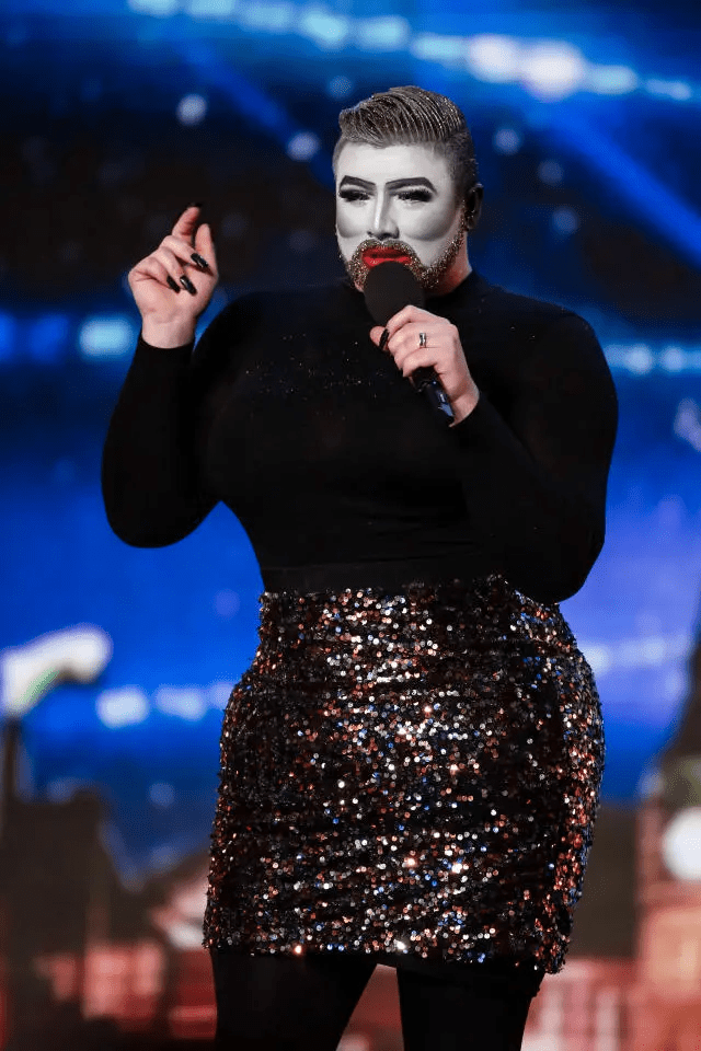 Person in black top and sequined skirt speaking into a microphone.