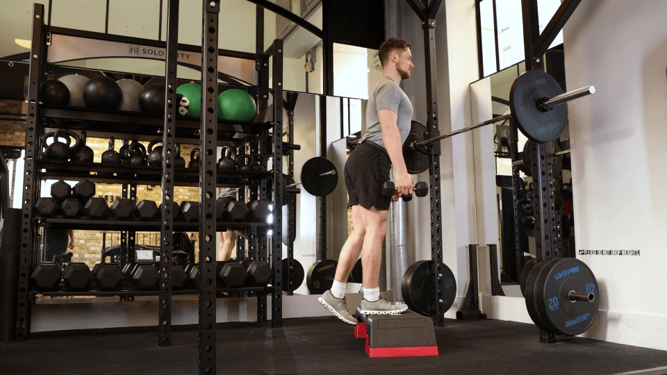 Man performing a single-leg dumbbell exercise in a gym.