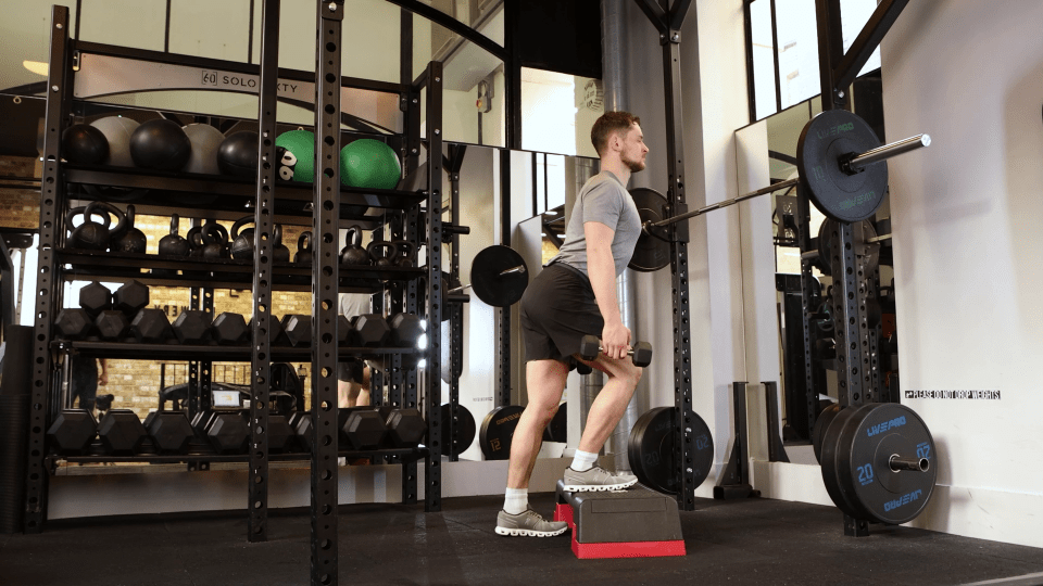 Man performing a dumbbell split squat in a gym.
