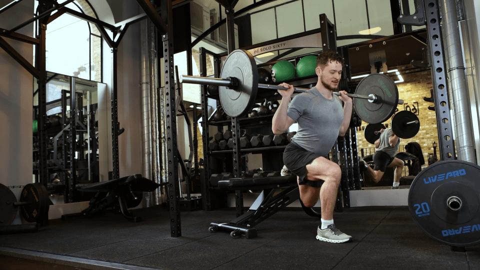 Man performing a barbell split squat in a gym.