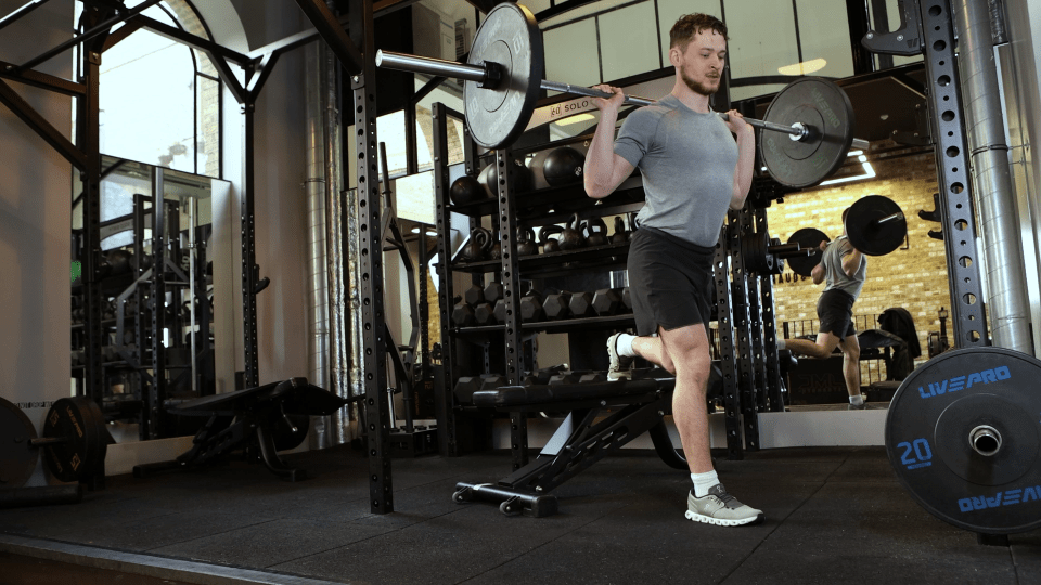 Man performing a barbell single-leg squat in a gym.