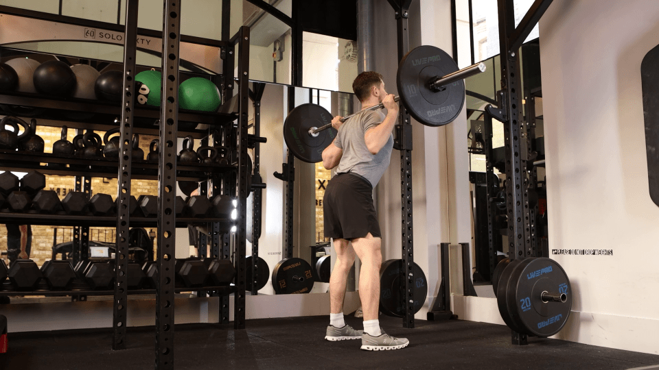 Man performing barbell back squats in a gym.