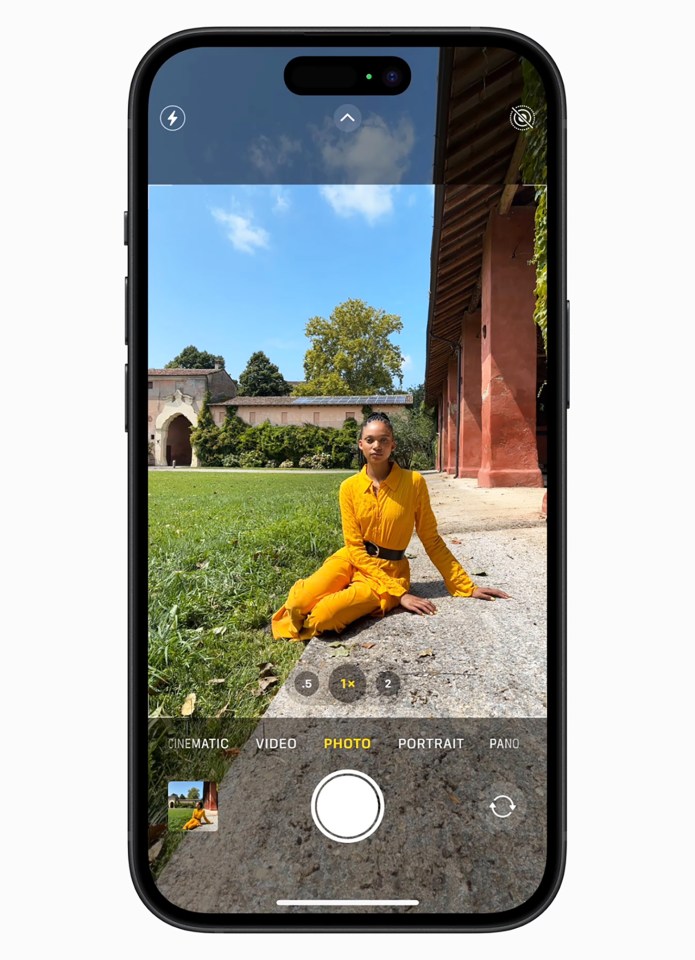 iPhone screen showing a photo of a person in a yellow outfit sitting on the ground in front of a building.